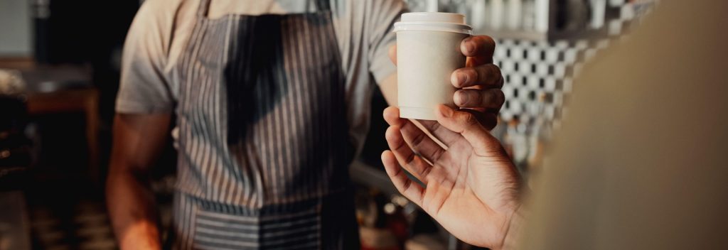 Waiter serving a cup of cold coffee to customer at counter in a café.