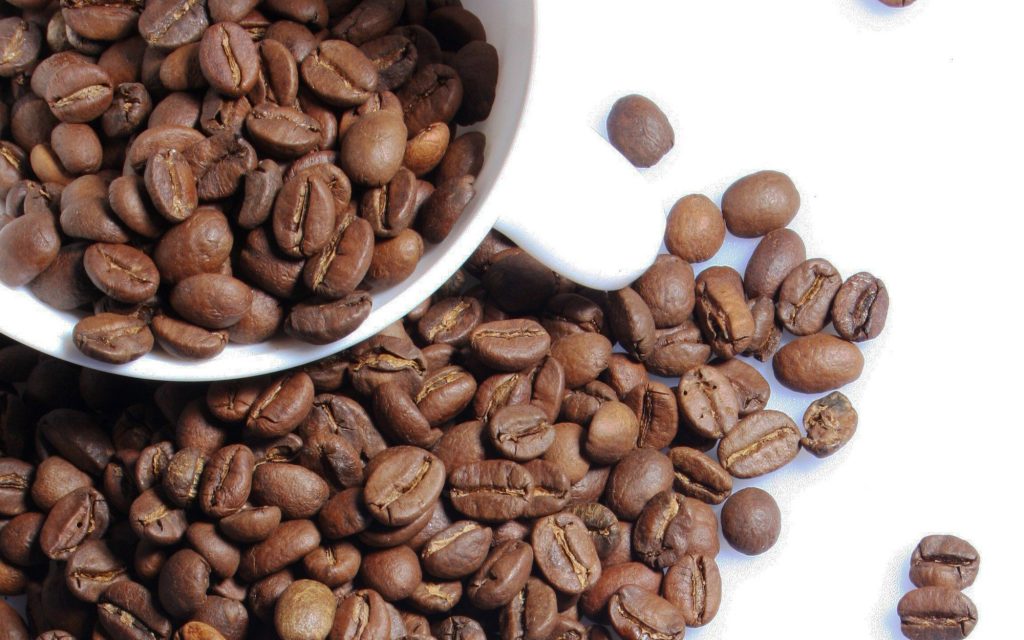 White cups filled with fresh coffee beans on a a white background